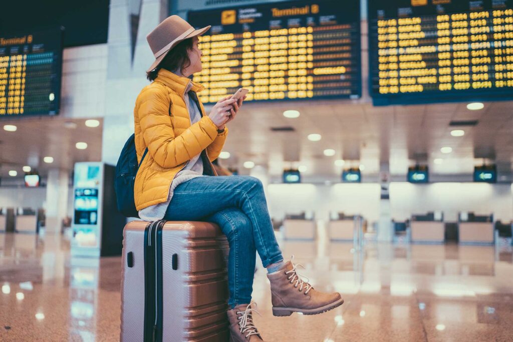 mujer sentada sobre maleta y buscando su vuelo